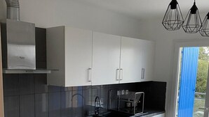 A modern kitchen with white cabinets, black countertops, a stainless steel range hood, and a black dishwasher. There is a window with a blue curtain and a door leading outside. - Spacious villa with pool in Nice (Nice)