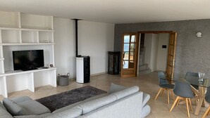 A modern living room with a grey sofa, a flat-screen TV, a black fireplace, and a dining area with a glass table and chairs. - Spacious villa with pool in Nice (Nice)