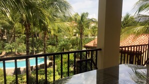 A balcony with a glass table and chairs overlooking a pool and lush greenery. - Pacifico Luxury 3B/2B condo, 10 minutes walk to the beach (Playa Del Coco)