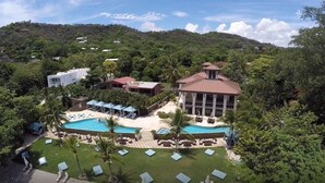 A resort with a swimming pool, lounge chairs, and a building with a red roof. - Pacifico Luxury 3B/2B condo, 10 minutes walk to the beach (Playa Del Coco)