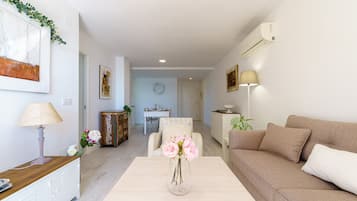 Una sala de estar moderna con un sofá, una mesa de centro y un florero. Se observa un comedor al fondo con una mesa y sillas.