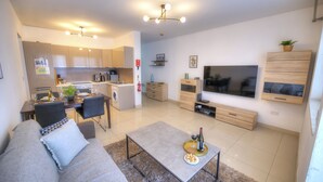 A modern living room with a sofa, coffee table, and a TV. There is a kitchen area with cabinets and a dining table. - Centrally located and modern apartment CKNI1 (Gzira)