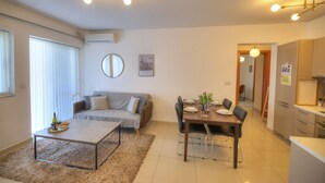 A modern living room with a sofa, coffee table, and dining area with chairs and a table set for two. - Centrally located and modern apartment CKNI1 (Gzira)