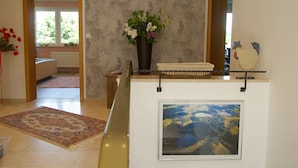 A room with a large window, a vase with flowers, a framed picture, and a rug on the floor. - Vacation apartment Maar-Idyll, quiet, modern vacation apartment with freedom of movement (Schalkenmehren)