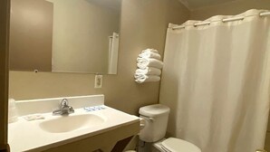 A bathroom with a sink, mirror, toilet, and a shower curtain. - Sunland Inn Motel (Ephrata)