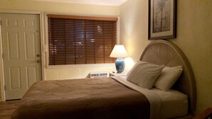 A neatly made bed with a brown cover, a bedside lamp, and a framed picture on the wall. - Sunland Inn Motel (Ephrata)