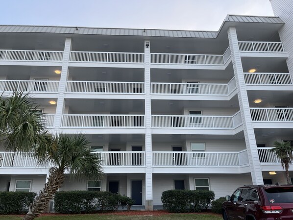 A multi-story building with balconies, a parking area, and a palm tree.
