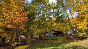 A cabin surrounded by autumn foliage, with a visible deck area and a path leading to the cabin.