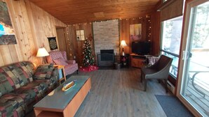A cozy living room with a wooden ceiling, a fireplace, a TV, and a Christmas tree.