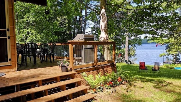 A wooden deck with outdoor seating, a grill, and a view of a lake.