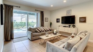 Ein modernes Wohnzimmer mit zwei Sofas, einem Couchtisch, einem Fernseher und einer Schiebeglastür, die auf einen Balkon führt.