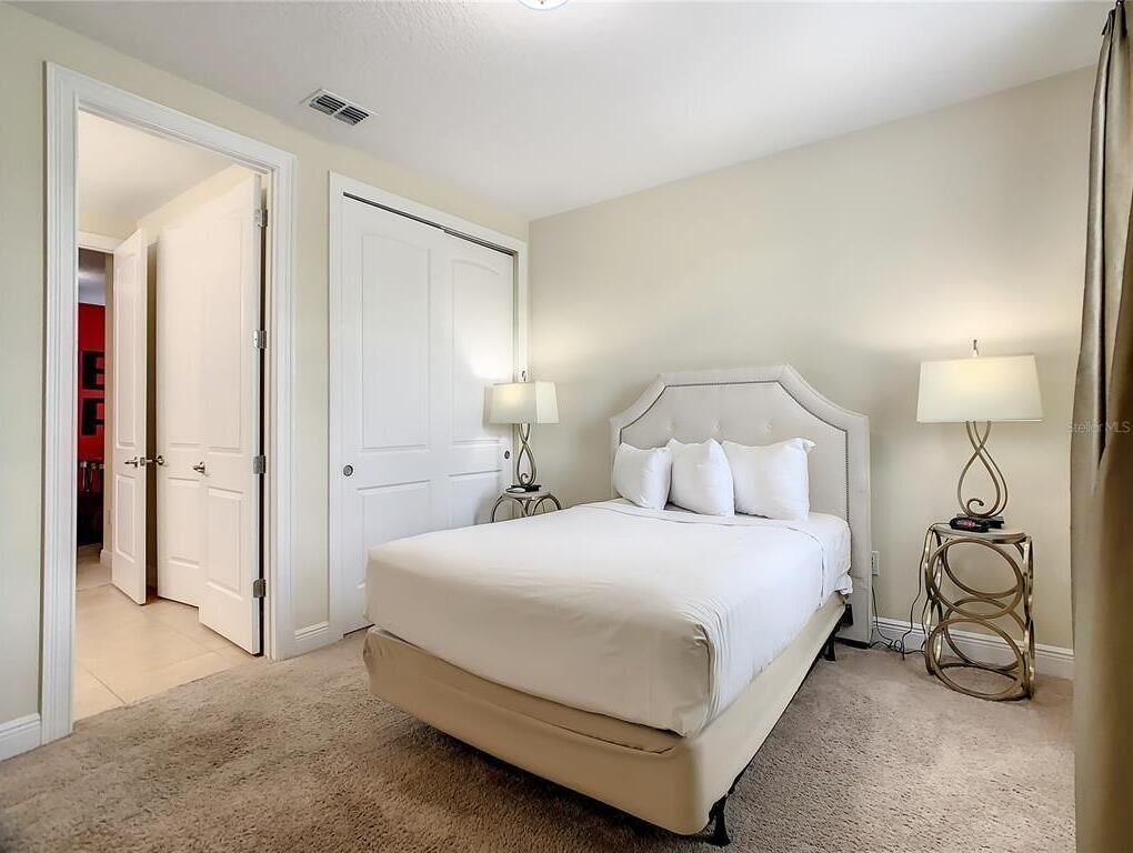 Une chambre à coucher avec un grand lit, deux tables de chevet avec des lampes, une porte et un sol recouvert d’une moquette.