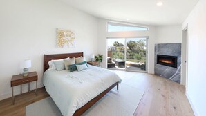 Un dormitorio moderno con una cama grande, una chimenea y un balcón con mobiliario exterior.