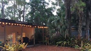 A covered outdoor area with string lights, a barbecue grill, and various plants. - Whispering Pines Guest House (Naples)