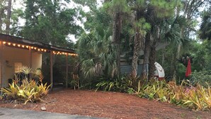A covered outdoor area with a dirt ground, surrounded by various plants and trees. - Whispering Pines Guest House (Naples)