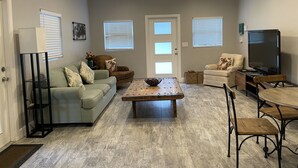 A spacious living room with a wooden coffee table, a sofa, a television, and a ceiling fan. - Whispering Pines Guest House (Naples)
