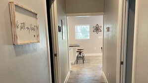 A hallway with a wooden floor, a bench, and a wall-mounted sign. - Whispering Pines Guest House (Naples)