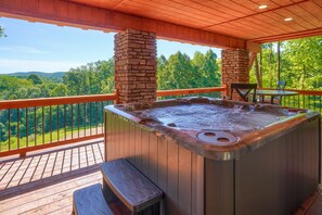 A hot tub on a wooden deck with stone pillars, overlooking a forested area.