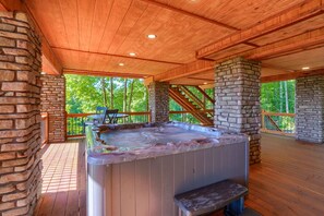Un bain à remous sur une terrasse en bois, avec des murs en pierre et une vue sur les arbres.