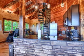Ein rustikales Blockhaus-Interieur mit Kamin aus Stein, Holzbalkendecke, Steinwand und Küchenbereich mit modernen Geräten.