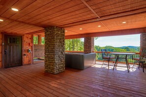 A wooden deck with a stone pillar, a hot tub, and outdoor seating.