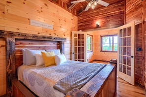 A wooden cabin bedroom with a bed, a sign on the wall, and a door leading outside.