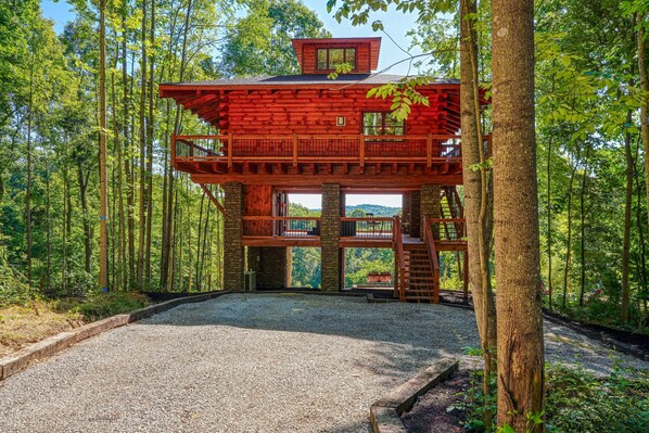 Une cabane en bois à plusieurs niveaux, avec une allée en gravier et entourée de forêt.