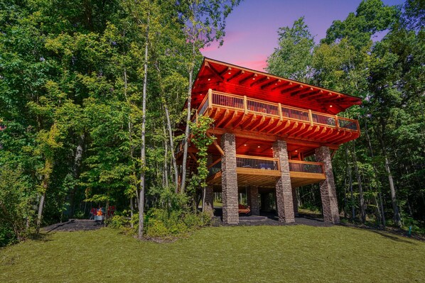 A multi-level wooden cabin with a balcony, surrounded by dense forest.