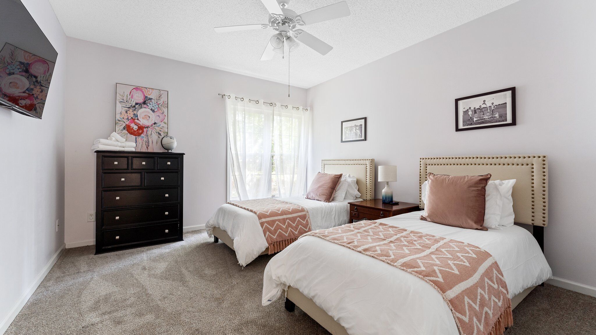 A bedroom with two beds, a dresser, a ceiling fan, and artwork on the walls.