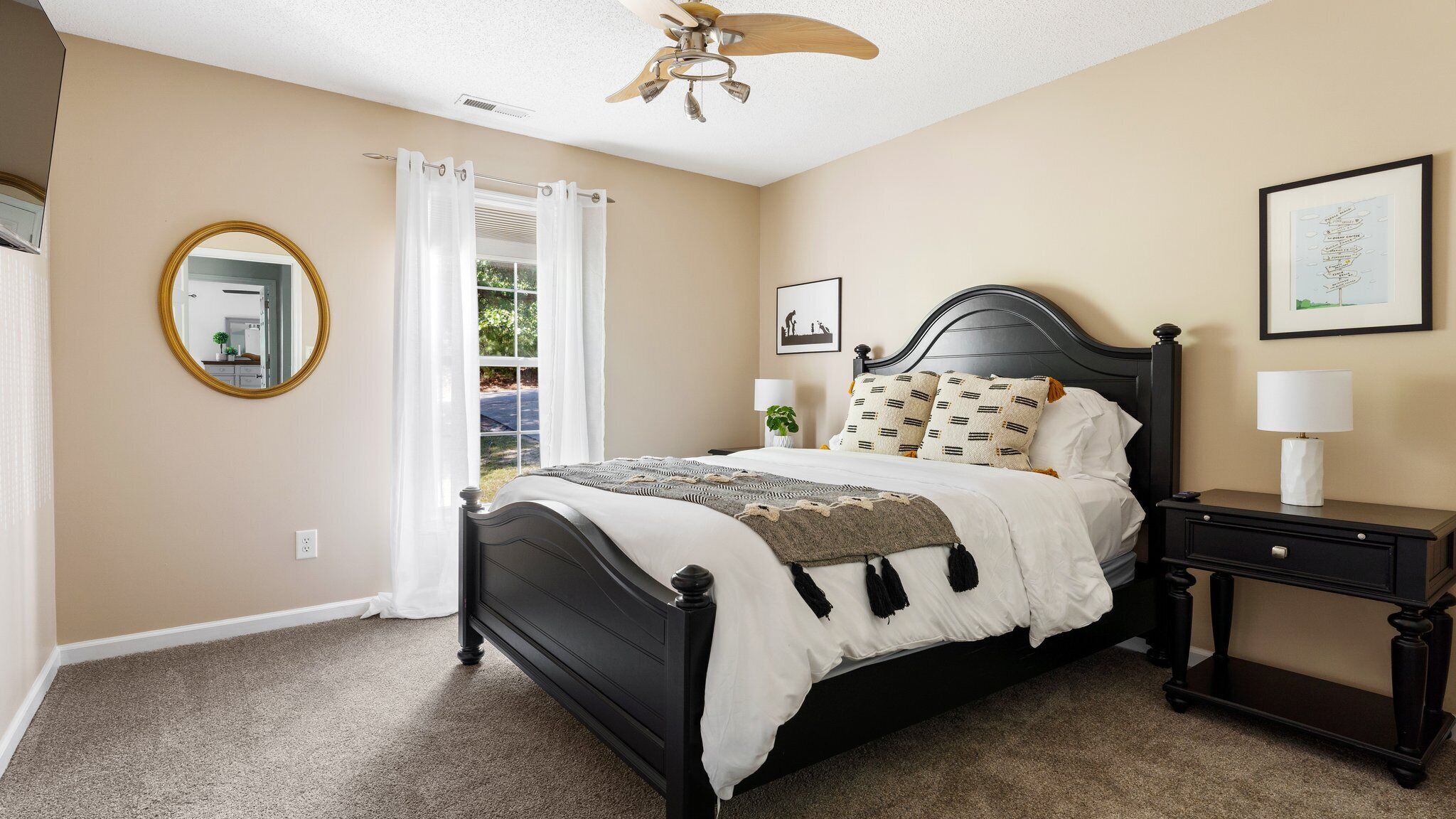 A bedroom with a bed, a nightstand, a ceiling fan, a mirror, and a window with curtains.