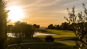 Ein Golfplatz mit Teich, Bäumen und einem Sonnenuntergang im Hintergrund.