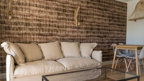 Ein Wohnzimmer mit einem beigen Sofa, einem Glastisch, einem Holzesstisch mit Stühlen und einer strukturierten Wand.