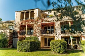 A multi-story building with balconies, a covered patio, and a well-maintained garden.
