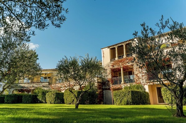 A two-story building with a balcony, surrounded by well-maintained hedges and trees.
