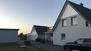 Une rangée de maisons blanches aux toits sombres, une allée pavée et une voiture garée.