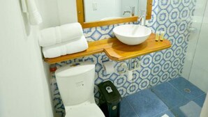 Un baño con un inodoro blanco, un tocador de madera con un lavabo y un espejo sobre el lavabo.