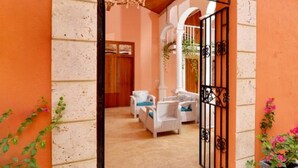 Una entrada con una puerta blanca, un portón negro y un piso de baldosas que conduce a un cuarto con un sofá blanco y una silla colgante.