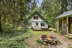 A cabin with a deck, surrounded by dense forest. - Sky One (Skykomish)