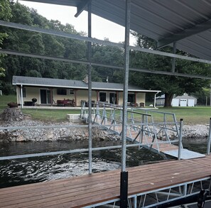 A covered dock with a wooden walkway leading to a house with a garage.