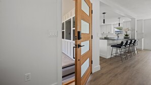 A modern kitchen with white cabinets, a wooden door, and a bar area with stools. - Lux Pool Home Close to Mayo & Jacksonville Beach! (Jacksonville)