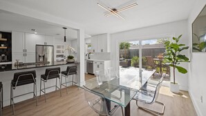 A modern kitchen with white cabinetry, a stainless steel refrigerator, and a glass dining table with bar stools. - Lux Pool Home Close to Mayo & Jacksonville Beach! (Jacksonville)