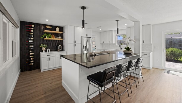 A modern kitchen with white cabinetry, a central island with bar stools, pendant lighting, and a wine rack. - Lux Pool Home Close to Mayo & Jacksonville Beach! (Jacksonville)