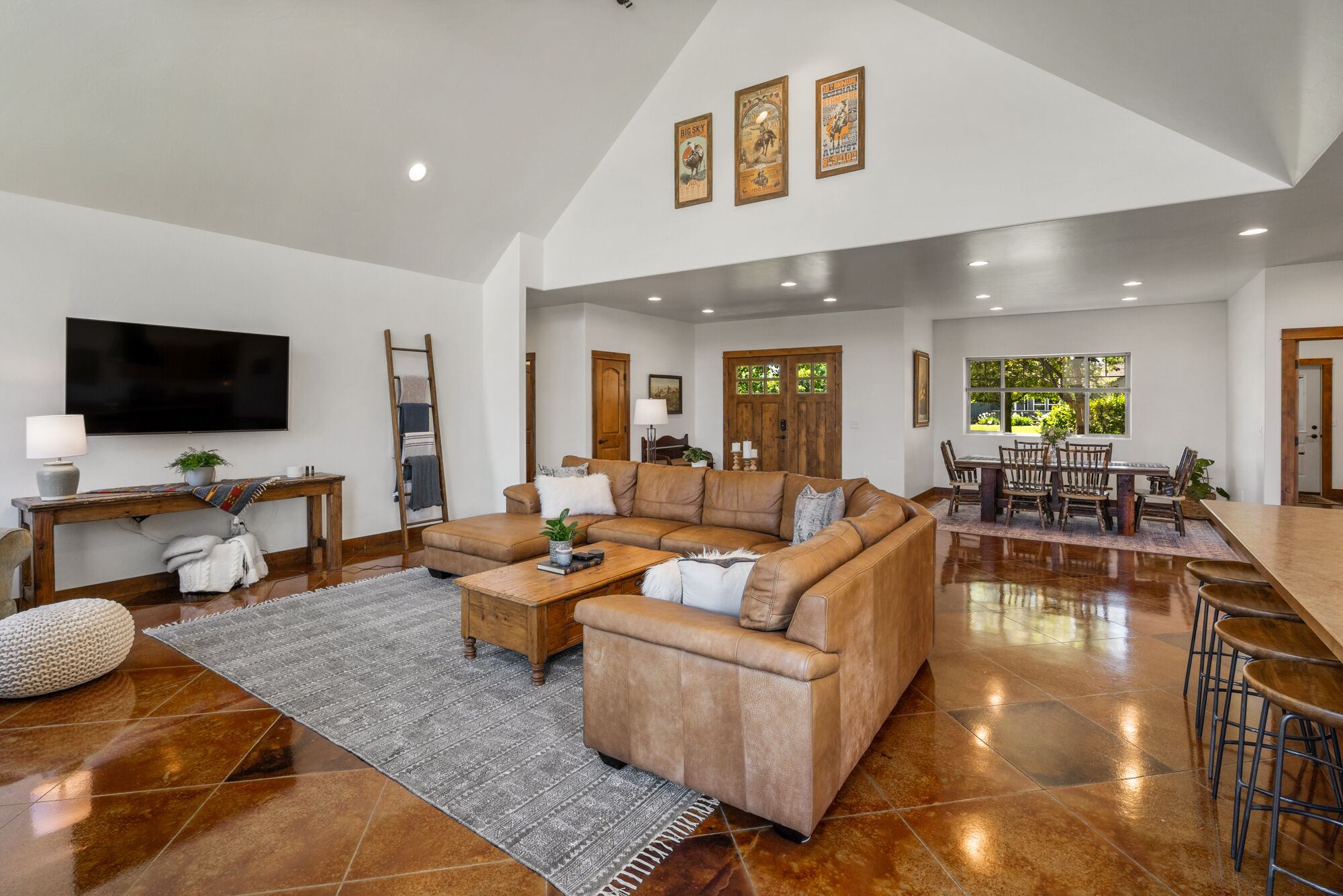 A spacious living room with a large sectional sofa, a dining area with a wooden table, and a TV mounted on the wall.