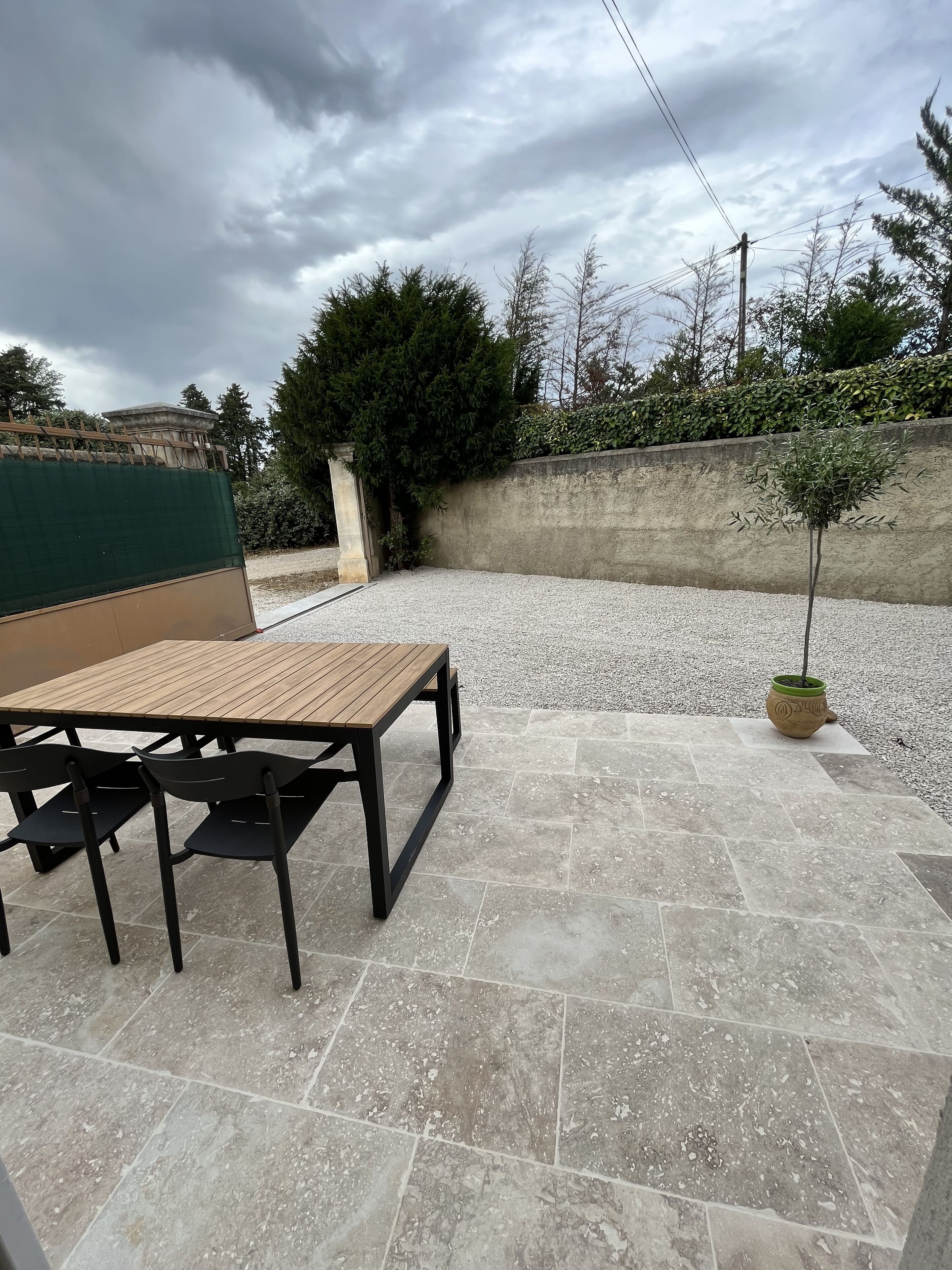 An outdoor patio with a wooden table and chairs, surrounded by a gravel area and a low concrete wall.
