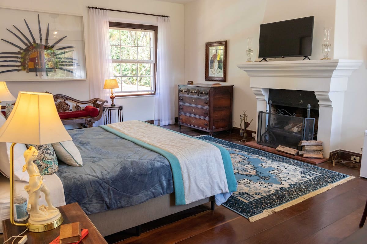 A bedroom with a bed, a dresser, a television, a fireplace, and a window with curtains.