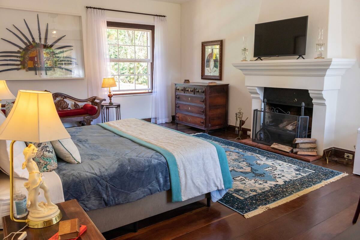 A bedroom with a bed, a dresser, a television, and a fireplace.