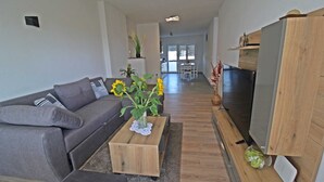 A modern living room with a grey sofa, wooden coffee table, and a TV stand.
