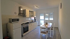 A modern kitchen with a microwave, stove, oven, and white cabinets. There is a dining table with chairs and a window with blinds.