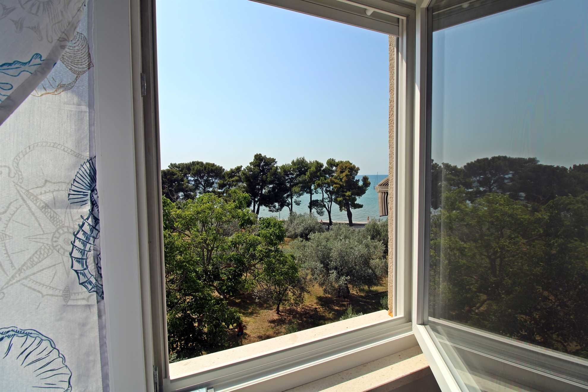 Vista des d'una finestra sobre una zona costera amb arbres i cel serè.
