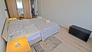 A bedroom with a bed, a wooden wardrobe, a small table with a lamp, and a black storage box.